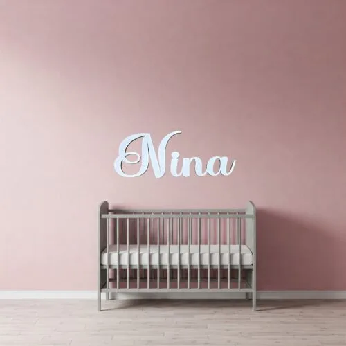 Prénom en bois "Nina" de couleur blanc, accroché au mur rose d'une chambre d'enfant.