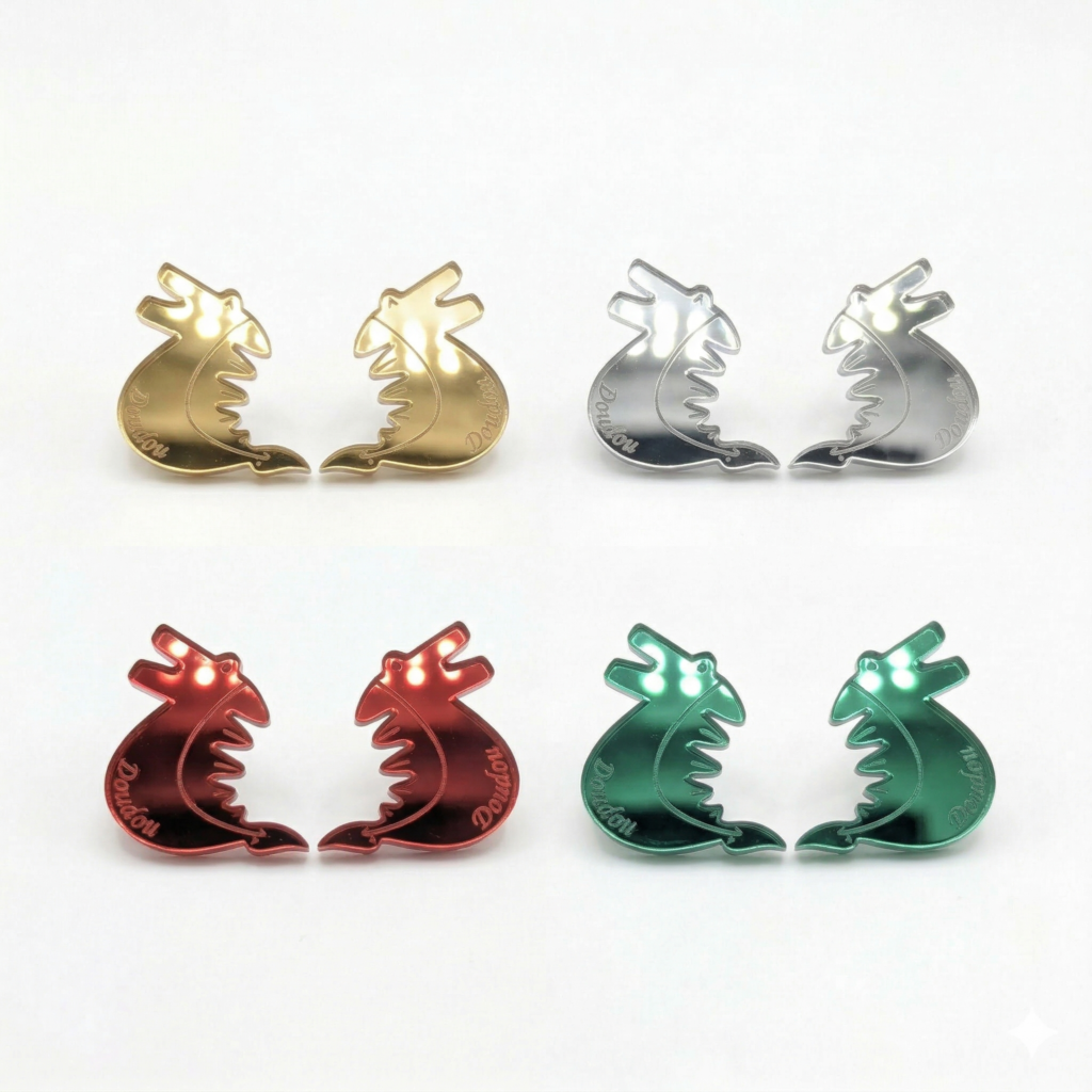 Photo gros plan de deux boucles d'oreilles en forme de dragon, inspirées de la Ducasse de Mons (Doudou), fabriquées en acrylique miroir coloré. Les dragons sont d'un vert émeraude vif avec des reflets métalliques.