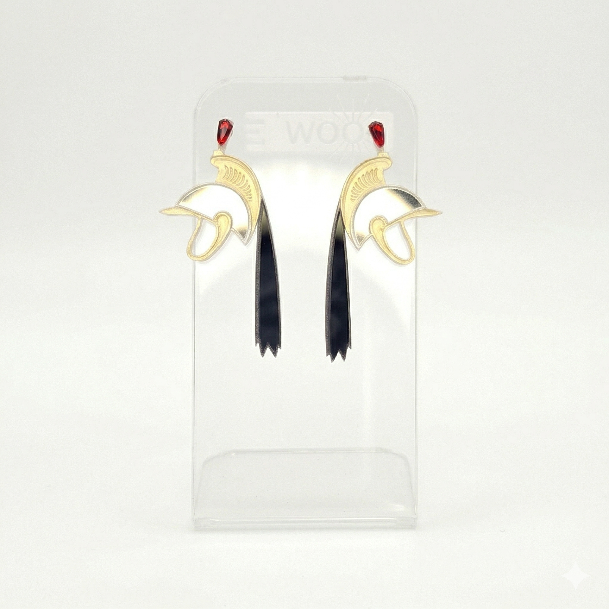 Boucles d'oreilles LEAWOOD en or et argent, représentant le casque de Saint-Georges porté lors de la Ducasse de Mons (Le Doudou), avec pierres rouges et pampilles noires. Vue de face sur présentoir.